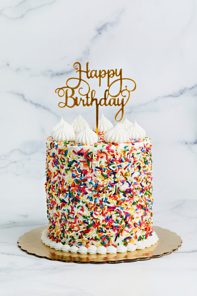 Birthday cake covered in sprinkles and Happy Birthday topper 