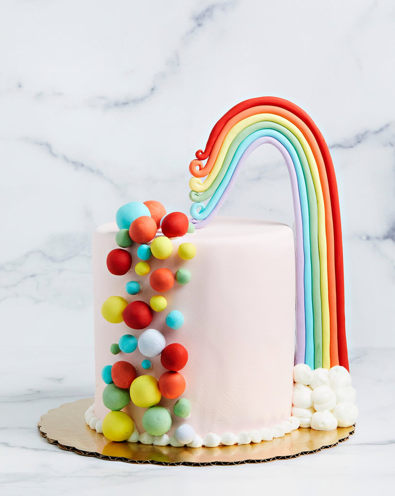 Pink cake with a rainbow starting in the top center and flowing down the right side