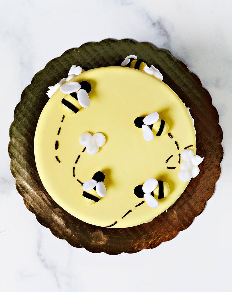 Top view of yellow cake with cute honey bees buzzing around